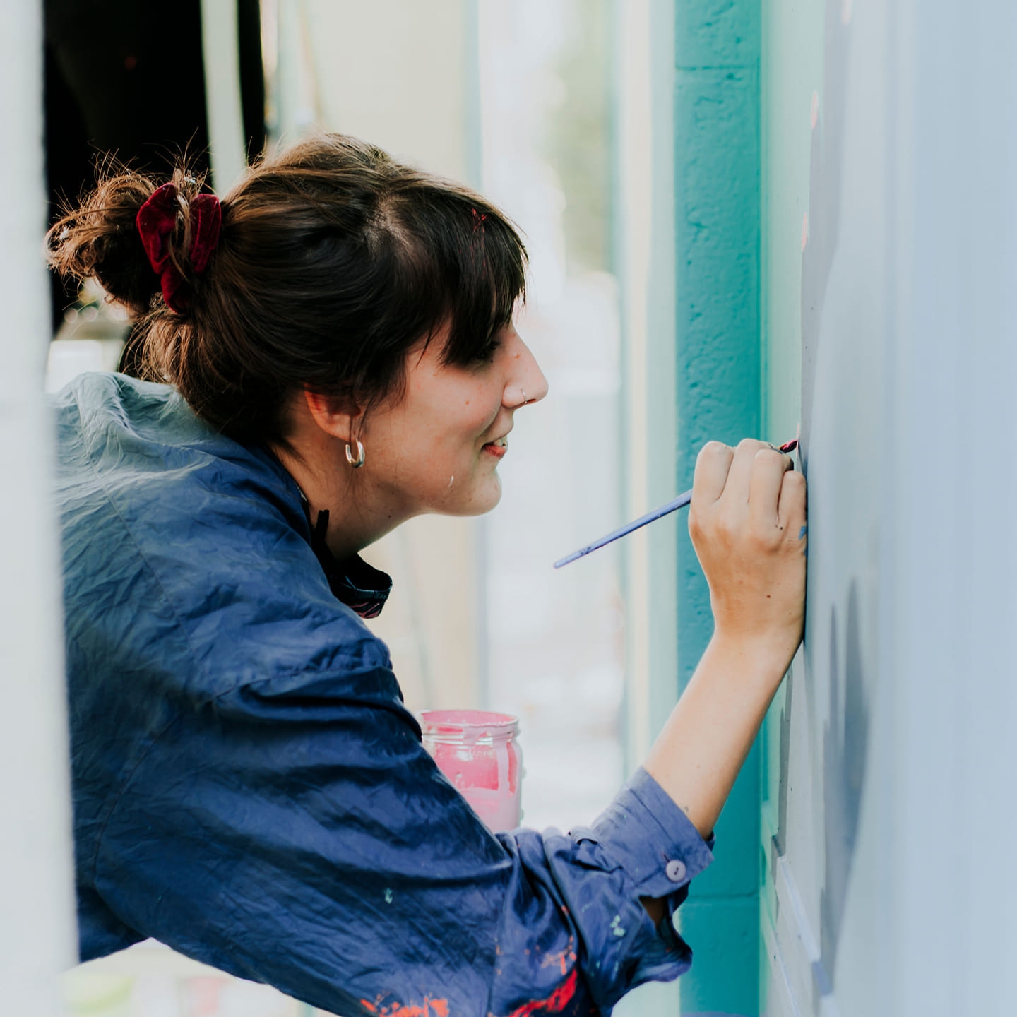 120362460_10224692897808467_4227322964878088768_o photo d'une jeune femme : camille loupe en train de peindre minutieusement un mur avec un pinceau très fin. Elle est souriante et à les cheveux attachés